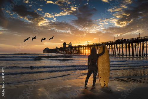 Fototapeta A female surfer admires a sunset near the Oceanside Pier.