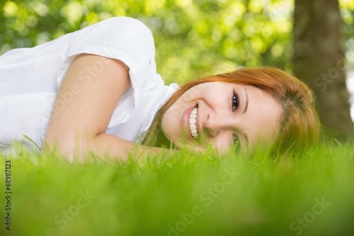 Pretty redhead smiling at camera lying on the grass