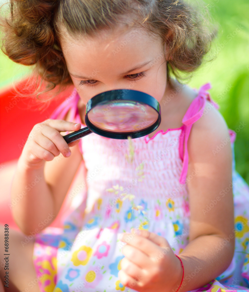Young girl is looking at flower through magnifier Young girl is looking at flower through magnifier