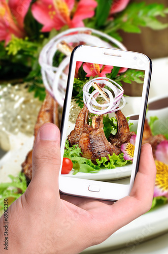 Hands taking photo roasted ribs  with smartphone