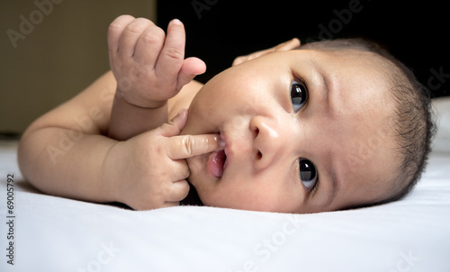 Close up of cute Asian baby boy sucking his finger on white bed