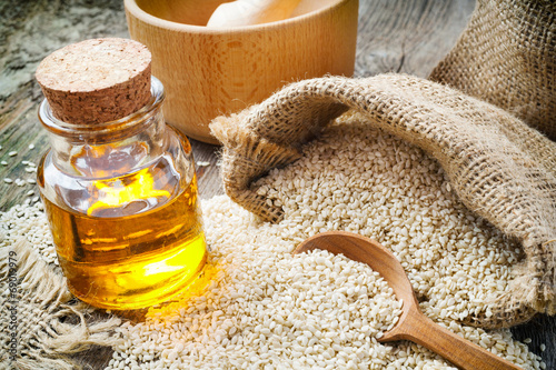 Фотография sesame seeds in sack and bottle of oil on rustic table