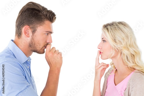 Young couple staying silent with fingers on lips