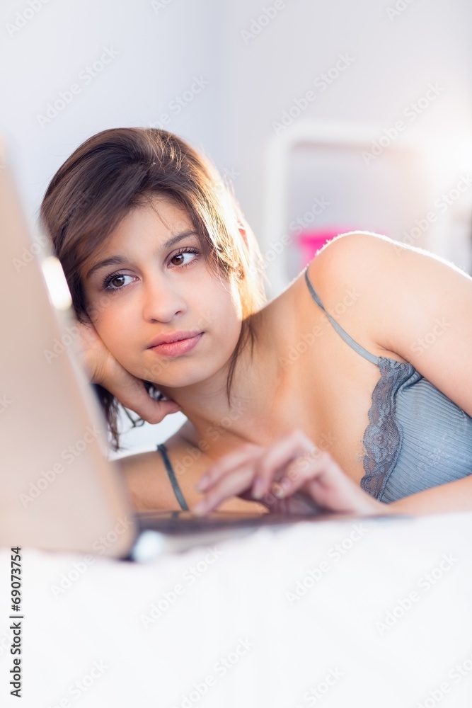 Obraz premium Beautiful brunette lying on bed using her laptop