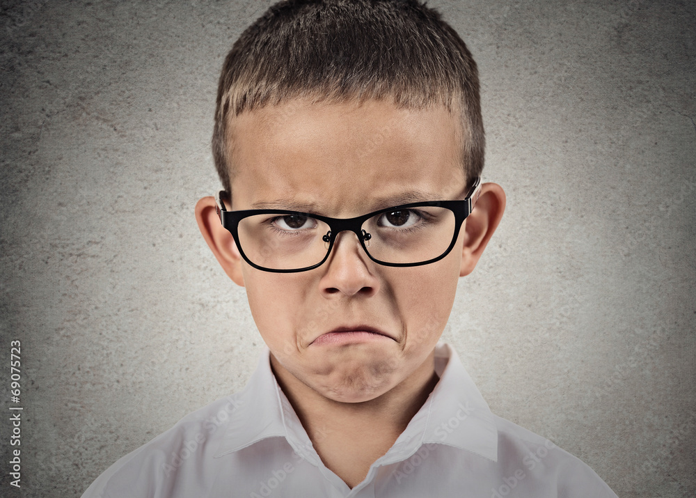 Unhappy sad, grumpy boy with glasses, grey wall background