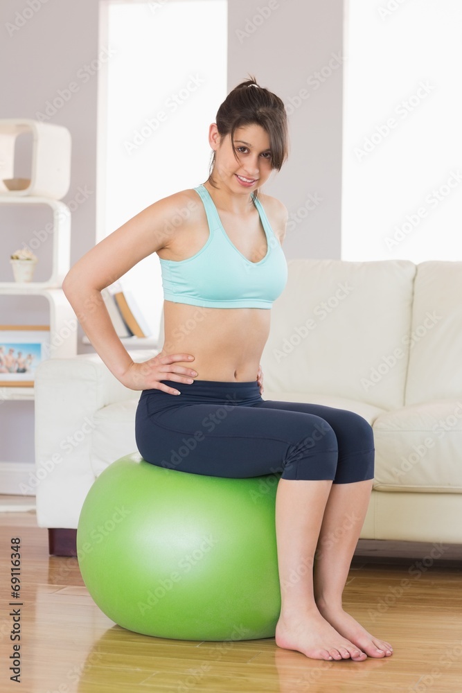 Fit brunette sitting on exercise ball smiling at camera