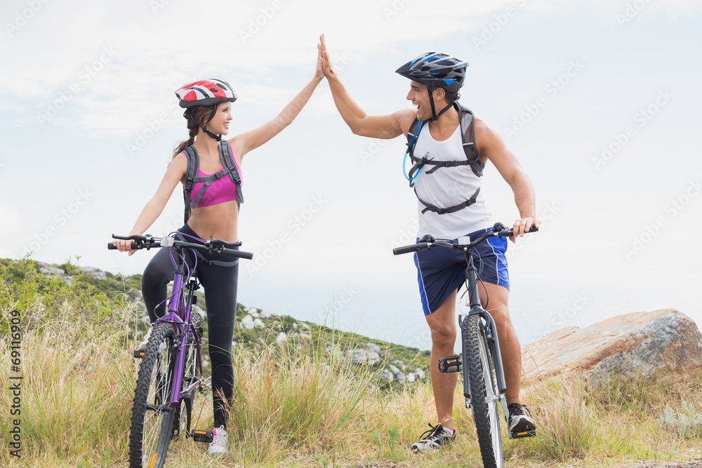 Athletic couple mountain biking while high fiving Athletic couple mountain biking while high fiving
