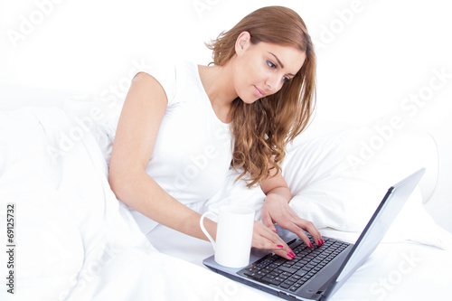 woman drinking coffee   tea using laptop computer in bed