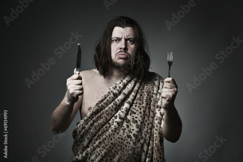 Hungry wild man wearing leopard skin hold fork and knife.