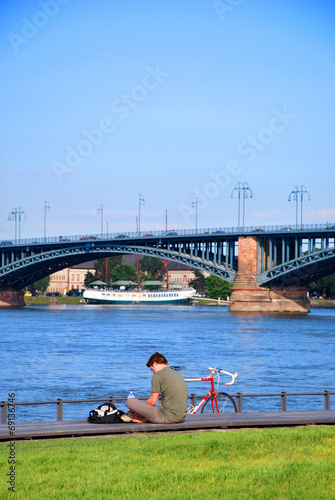 Young cyclist resting on a bank of a river and reading a book © ShiningBlack