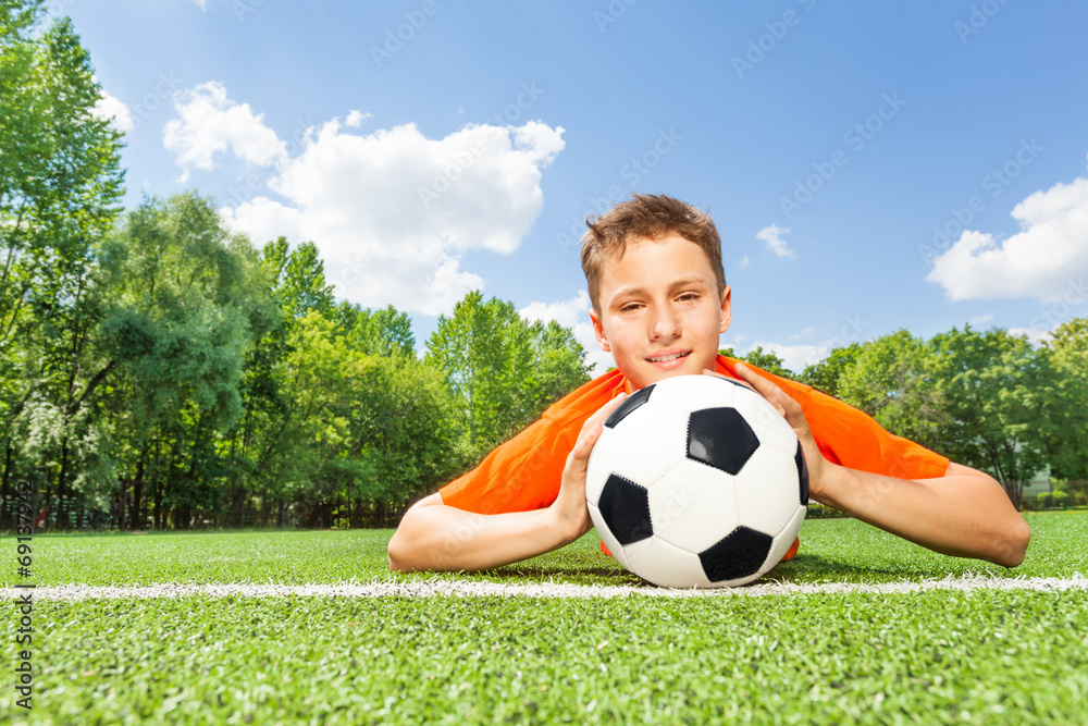 Obraz premium Happy boy holding football lays on green grass