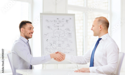 two smiling businessmen shaking hands in office