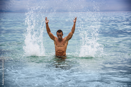 Handsome young bodybuilder in the sea  splashing water up