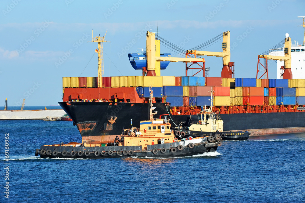 Tugboat assisting container cargo ship to harbor quayside