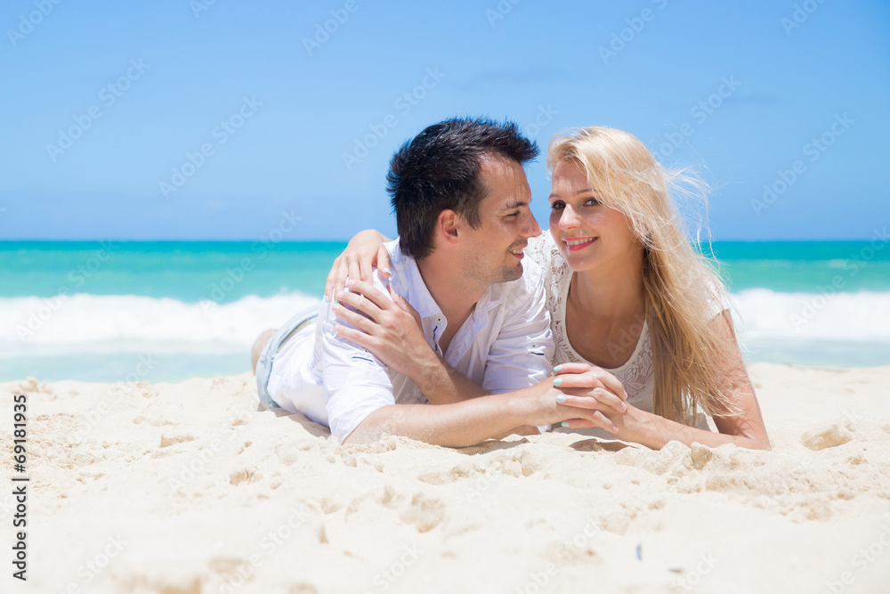 Cheerful couple embracing and lying on the beach on a sunny day