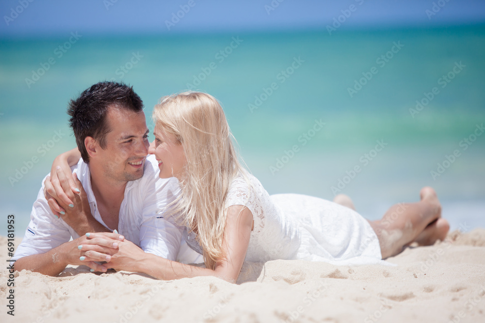 Cheerful couple embracing and lying on the beach on a sunny day Cheerful couple embracing and lying on the beach on a sunny day