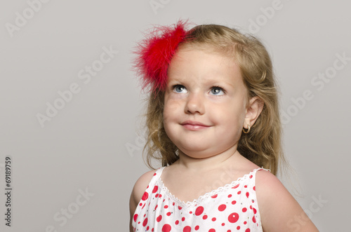 Little adorable blonde girl with a red flower in hair smilling