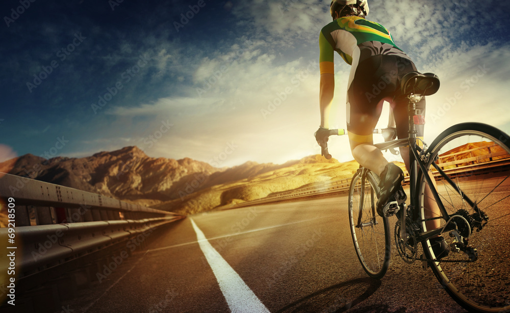 Cyclist riding a bike on an open road to the sunset - obrazy, fototapety, plakaty 
