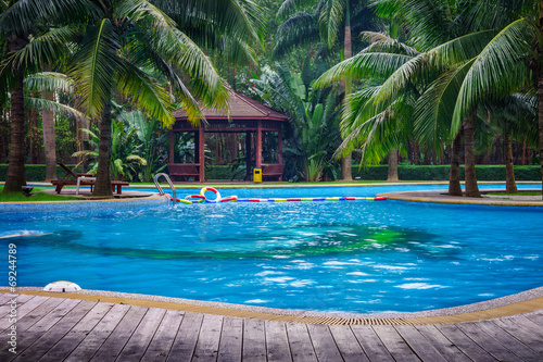 Swimming pool with hut and wooden pool deck in garden of resort