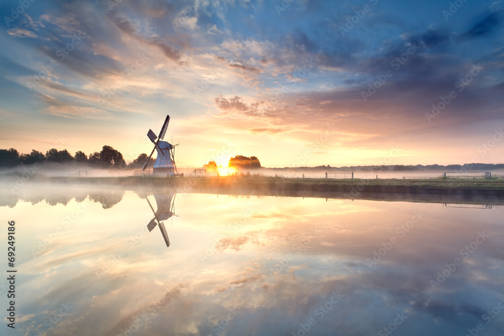 misty sunrise over windmill by river