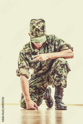 soldier with hidden face in green camouflage uniform and hat kne