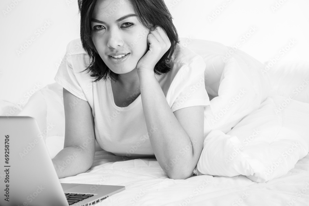 Smiling woman using a laptop while lying on her bed Smiling woman using a laptop while lying on her bed