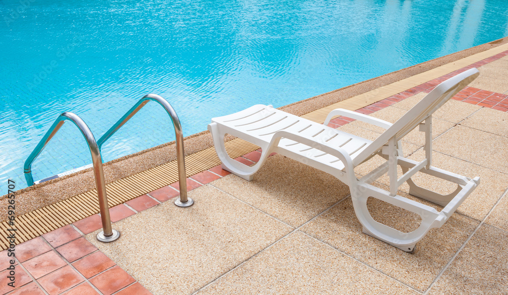 Relaxing beach chair beside grab bars ladder and blue swimming p Relaxing beach chair beside grab bars ladder and blue swimming p