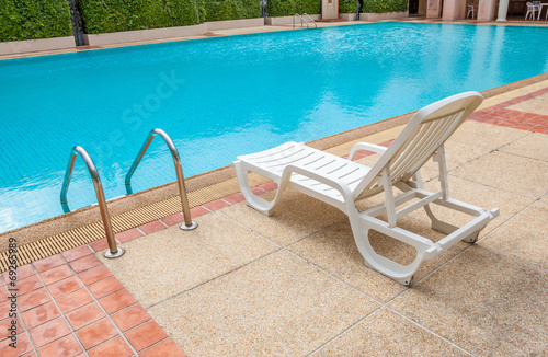 White lounge chair at the pool side near ladder, blue swimming p