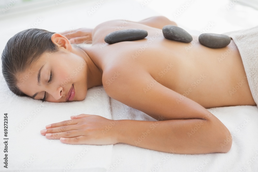 Beautiful brunette enjoying a hot stone massage - obrazy, fototapety, plakaty 