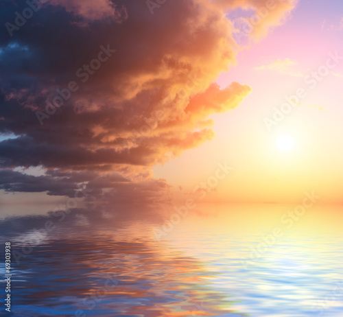 Sky with clouds and sun reflected in water surface.
