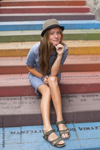 Cute young girl in a hat sitting on the stairs outdoors.