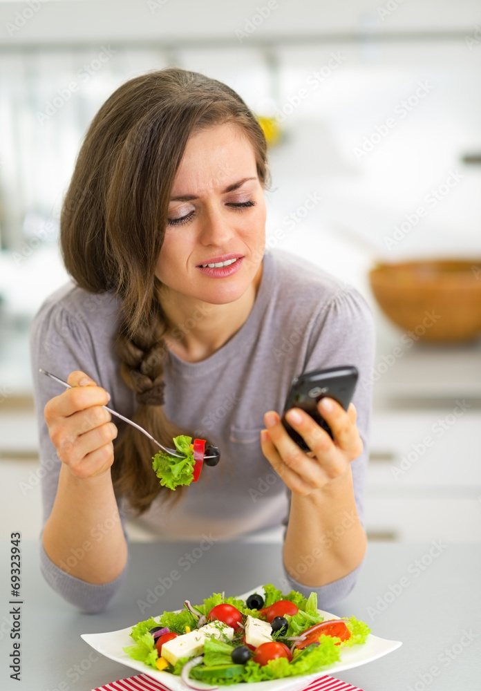 Young woman eating in kitchen and writing sms