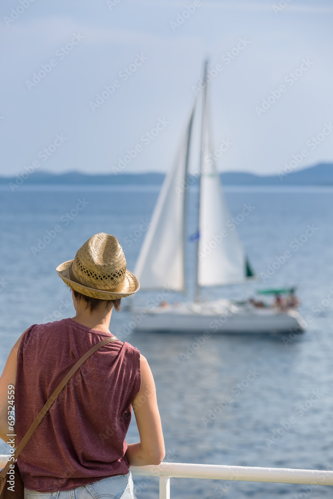 Female passenger on the deck of the ferry watching the sailboat
