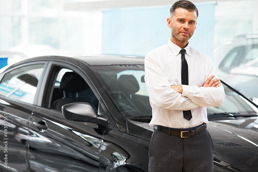 Salesman Stands Near Brand New Car. Car Showroom Salesman Stands Near Brand New Car. Car Showroom