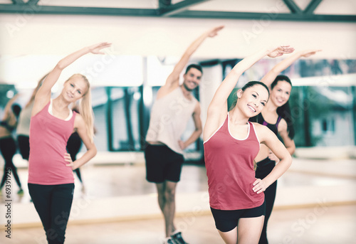 Fototapeta Naklejka Na Ścianę i Meble -  group of smiling people stretching in the gym