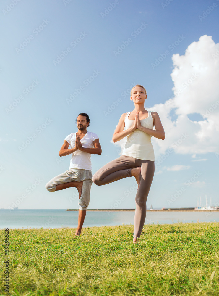 smiling couple making yoga exercises outdoors