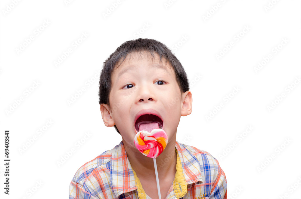 little Asian boy eating candy in his hand, isolated on a white b little Asian boy eating candy in his hand, isolated on a white b