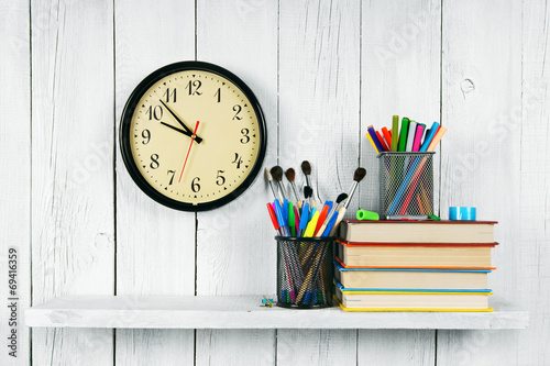 Watches, books and school tools on wooden shelf.