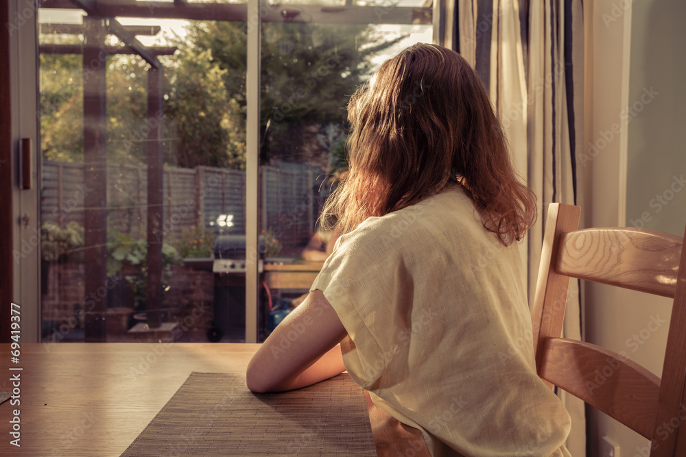 Young woman sitting at table and looking out the window Young woman sitting at table and looking out the window