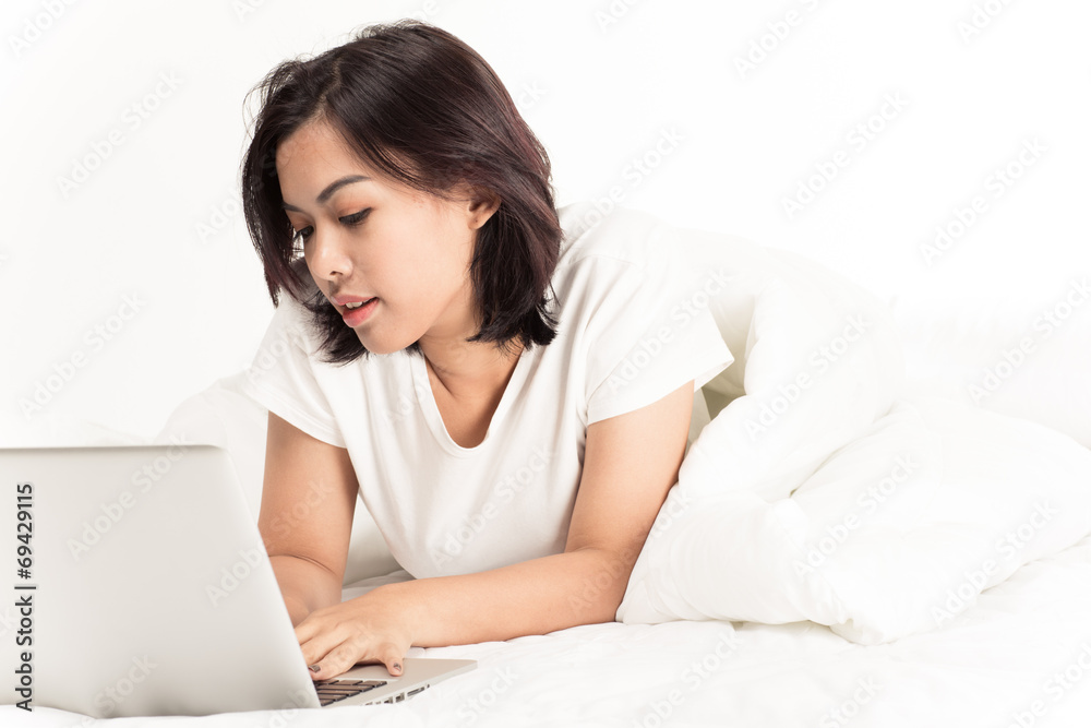 Smiling woman using a laptop while lying on her bed Smiling woman using a laptop while lying on her bed