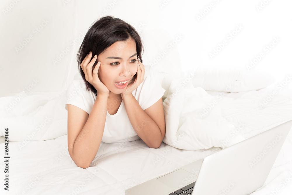 Smiling woman using a laptop while lying on her bed Smiling woman using a laptop while lying on her bed
