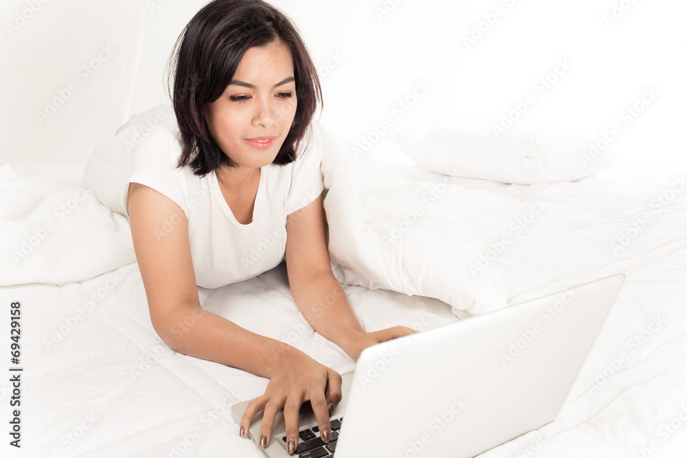 Smiling woman using a laptop while lying on her bed Smiling woman using a laptop while lying on her bed