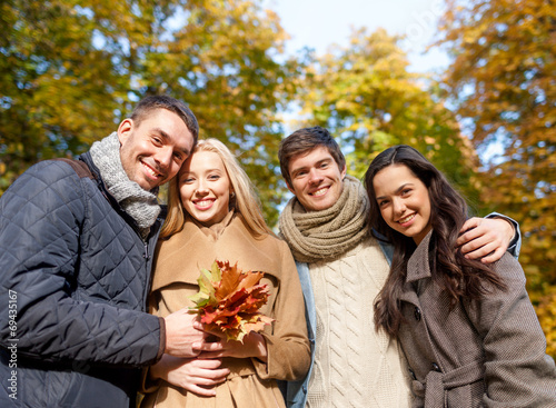 group of smiling men and women in autumn park