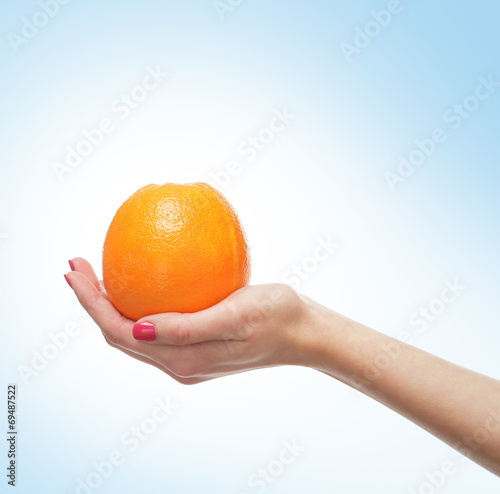 Beautiful female hands with an orange on light blue