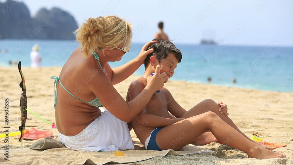 mother applying sunscreen to son on the beach at summertime mother applying sunscreen to son on the beach at summertime