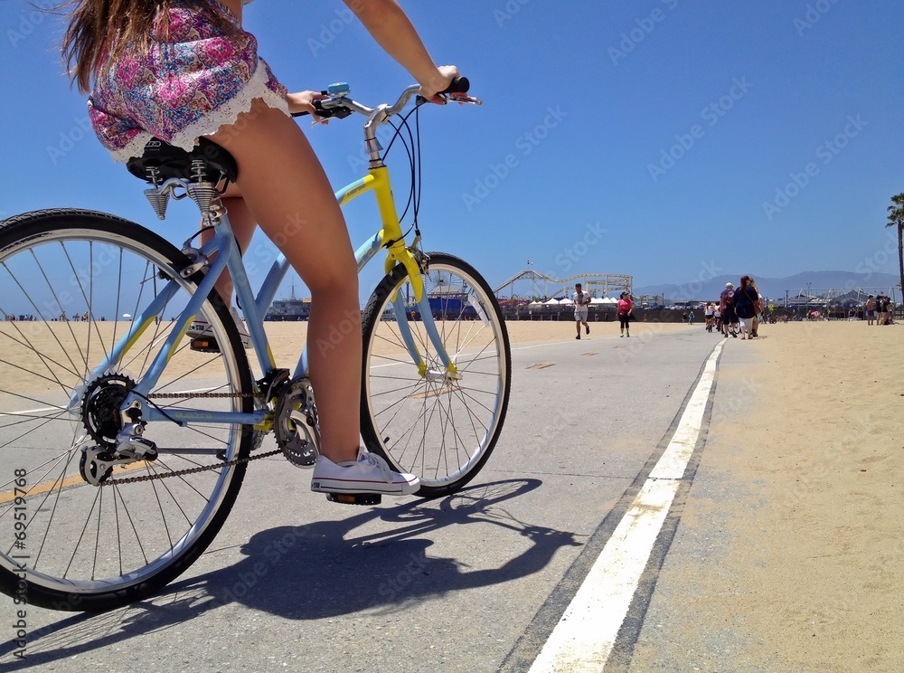 Obraz premium Pretty Woman riding a bicycle along Santa Monica Beach pathway