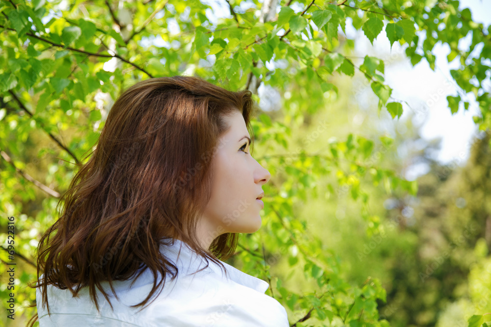 The girl looks upwards among green foliage
