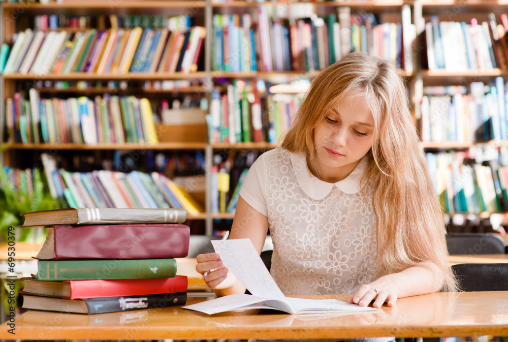young female student doing assignments in library young female student doing assignments in library