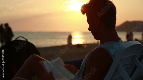 attractive young man reading a book on the beach photo