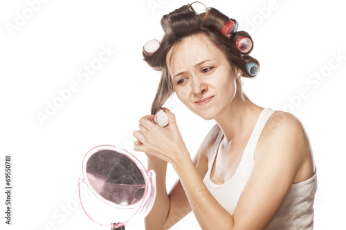 nervous young woman without make-up curls her hair with curlers